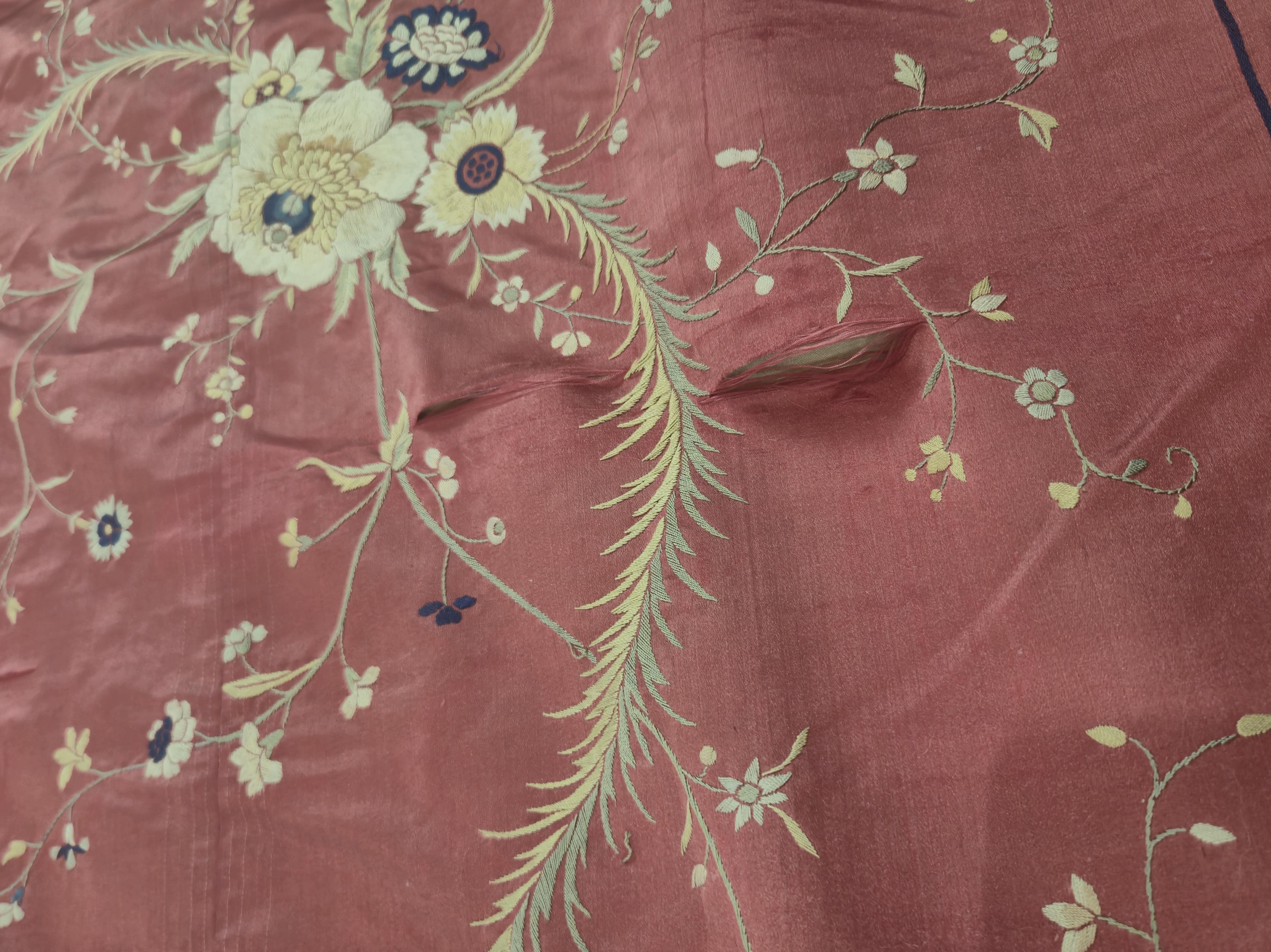 A Chinese 19th century Qing Dynasty crimson red silk embroidered hanging. Embroidered with sprays and swags of flowers and foliage, depicting prosperity and fortune, around a central stylistic sun motif, depicting perfec
